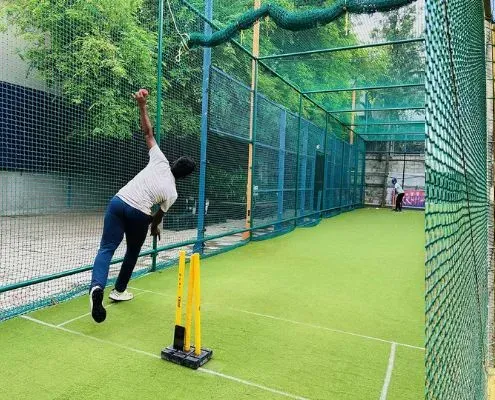 Bowler in a netted cricket practice lane with artificial turf and stumps