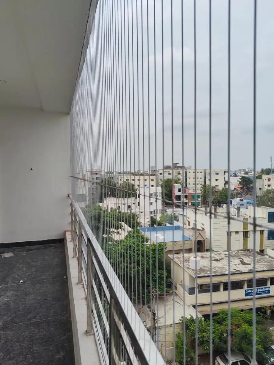 Vertical invisible grills along a long upper-floor balcony overlooking houses and trees