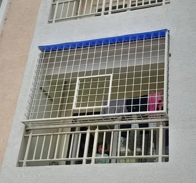 Apartment balcony boxed in by a white welded MS grill cage with a sheet roof on top