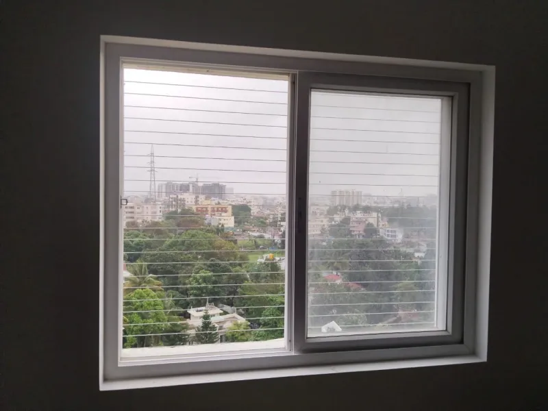 Horizontal invisible grill ropes behind a sliding window, looking out over trees and city buildings
